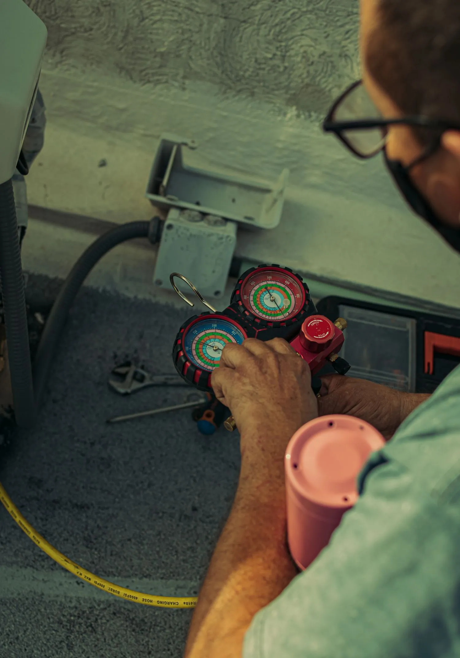 Close view of a hand holding refrigerant gauges beside an outdoor air conditioning unit