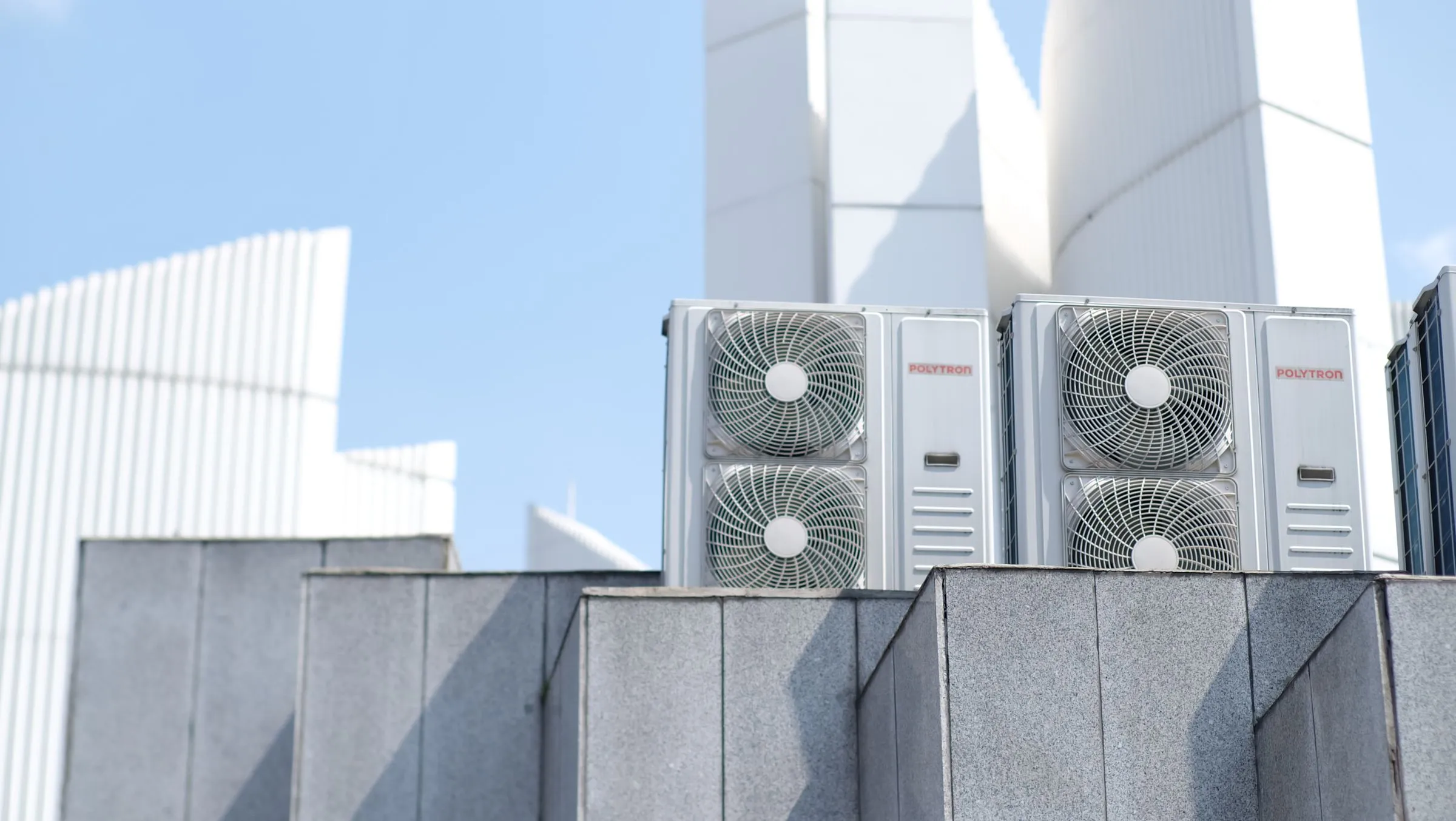 Two outdoor air conditioning units on a rooftop against a clear blue sky