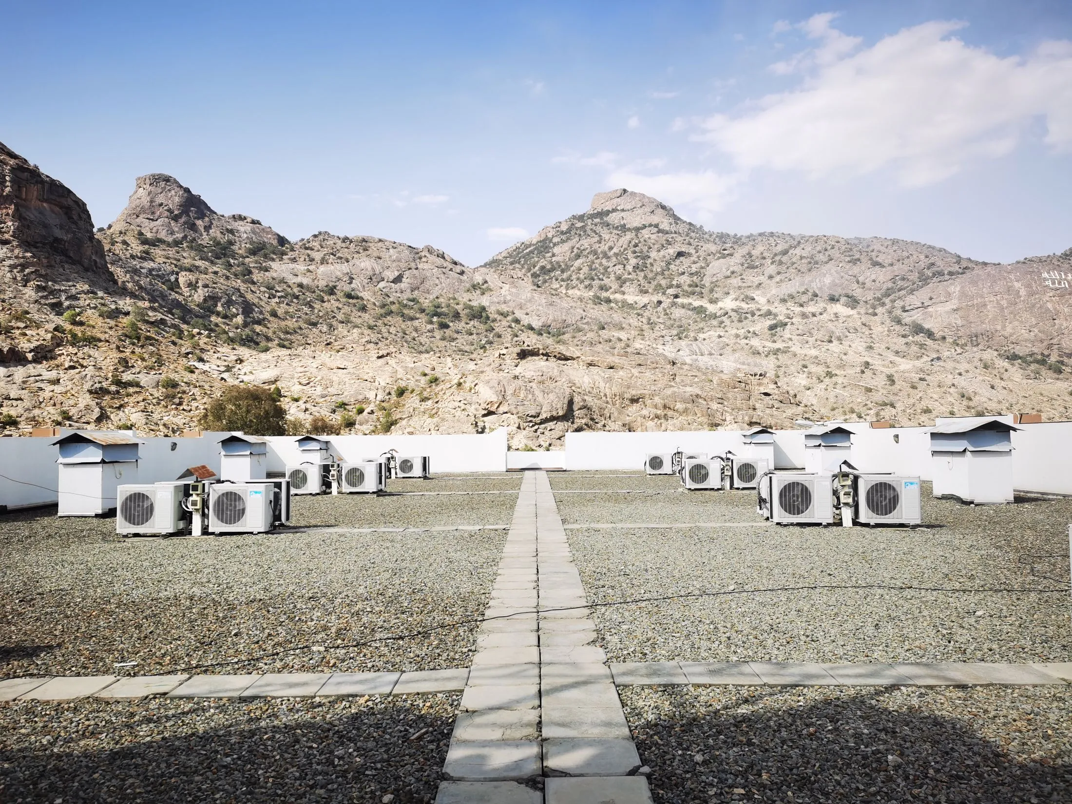 Rows of air conditioning units on a flat rooftop with hills in the distance