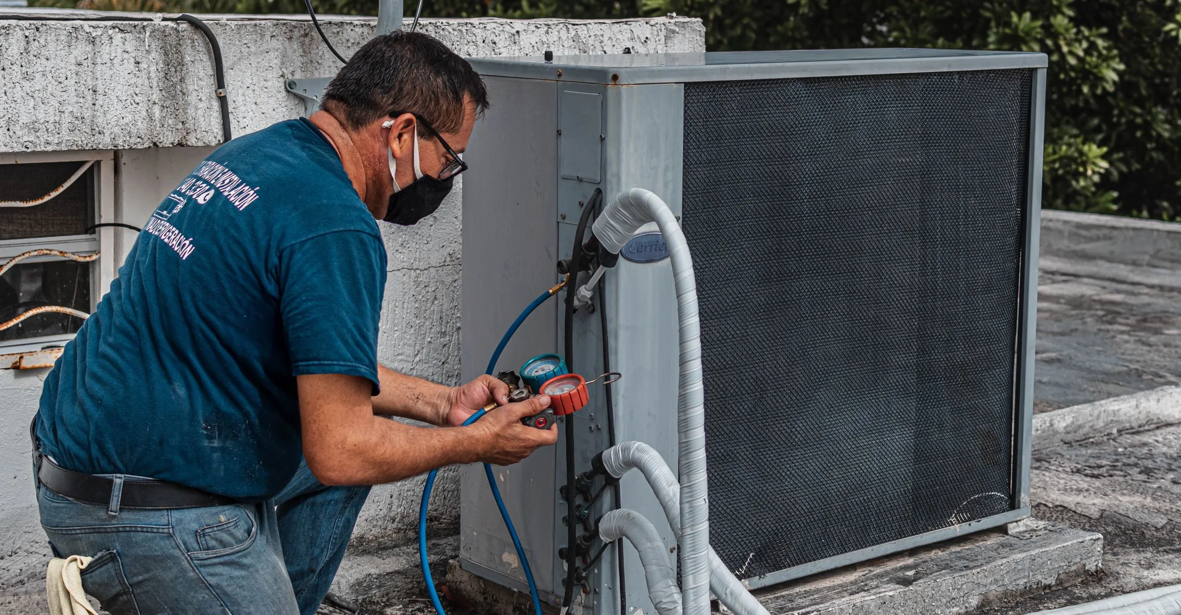 A technician connecting gauges and hoses to an outdoor air conditioning unit
