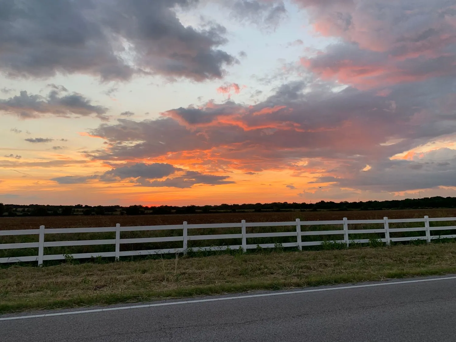A Texas pasture with a white fence at sunset under a red and orange sky